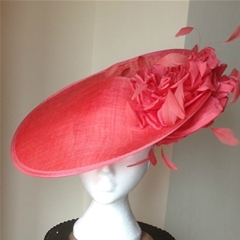 coral tilted disc with floral detail and coque feathers above and below brim. set on a headband. also comes in other black with yellow flower, black with silver flower, ivory, navy, red, plain black, royal blue or fuschia pink.